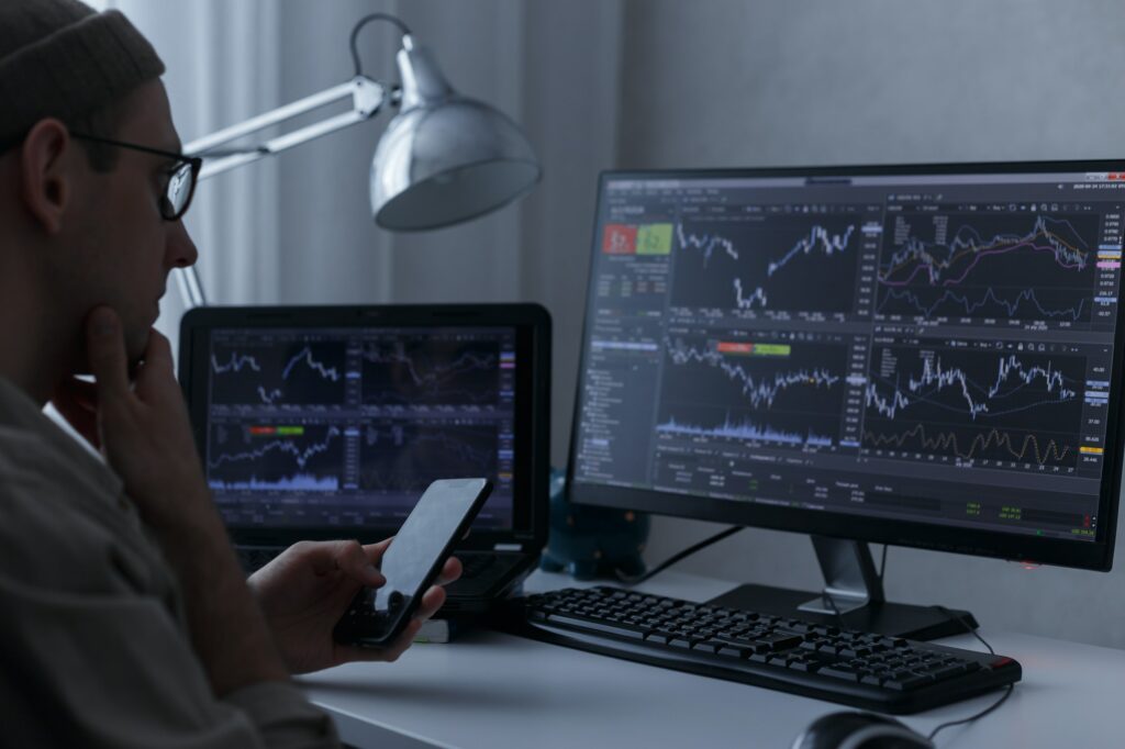 Trader analysing financial graph and stock statistics on monitors at his home workplace